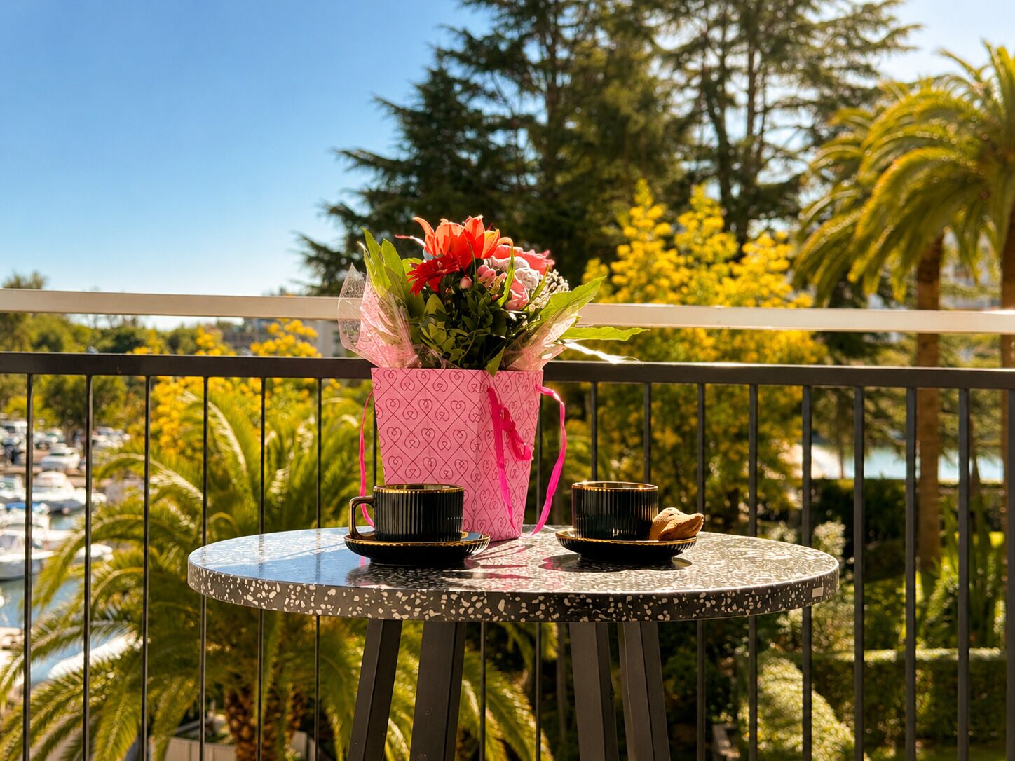 A balcony with a table, a pink heart-patterned gift box, and a bouquet of flowers.
