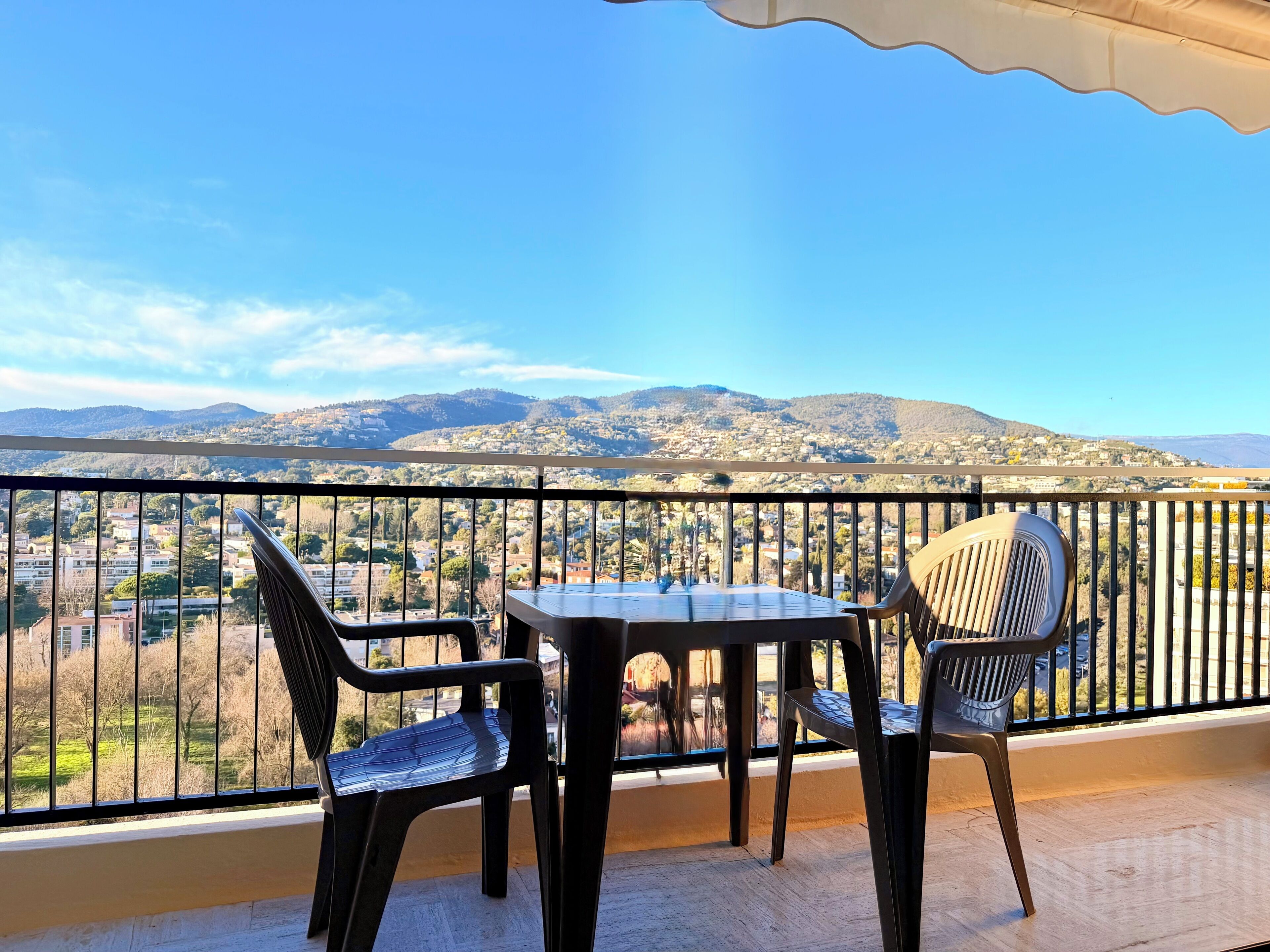 Un balcon avec une table et des chaises, offrant une vue sur le paysage urbain et les montagnes.