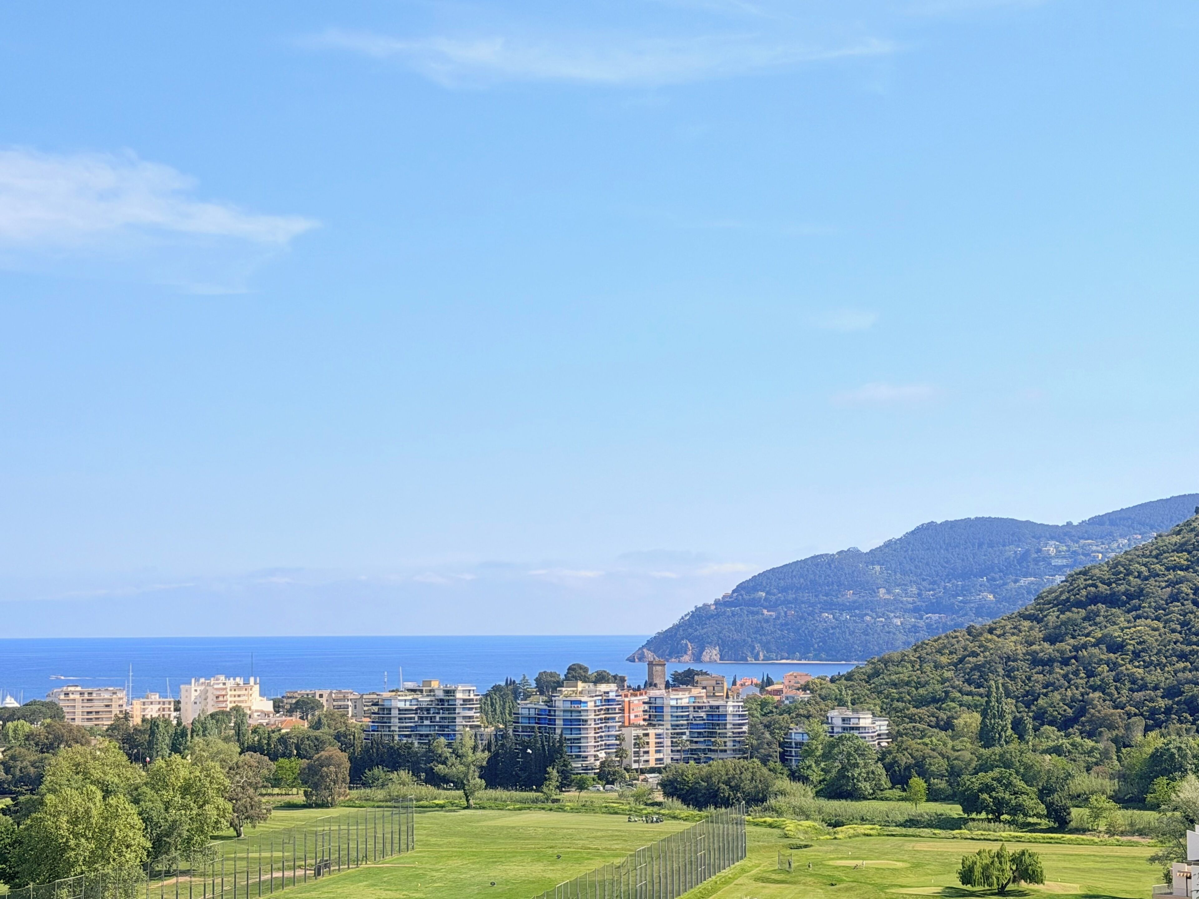 A coastal cityscape with modern buildings, a clear sky, and a view of the sea.