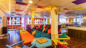 A colorful interior with a long sofa area, a chess table, and a fan. - ZoukStayz (Rishikesh)