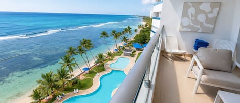 Un balcon avec vue sur une plage, une piscine et un espace détente.