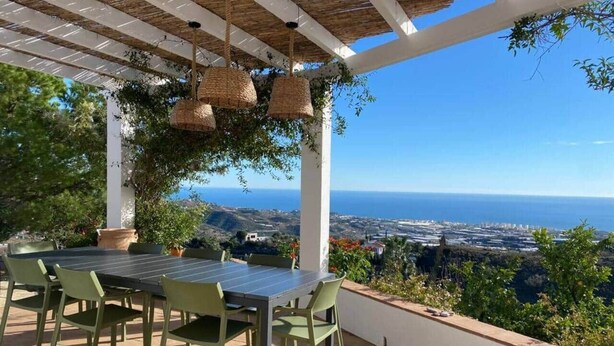 Un patio al aire libre con una mesa y sillas, con vistas a un paisaje costero.