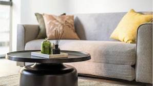 A modern living room with a grey sofa, a yellow pillow, and a small table with a green vase and incense sticks. - Skyscraper Cinema - Dream a thousand city lights (Brisbane City)