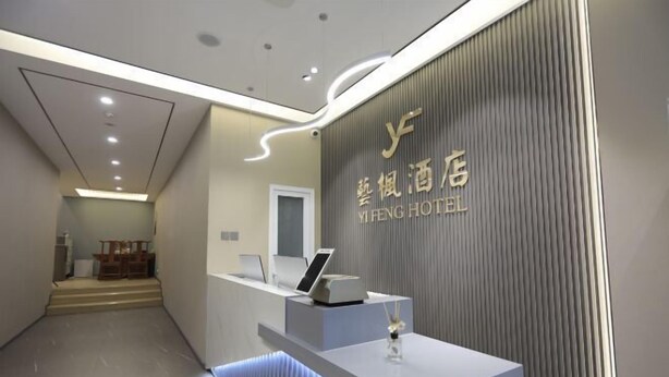 A reception area with a modern design, featuring a reception desk, a wall-mounted sign with hotel name, and a staircase leading to another floor. - YI FENG HOTEL (Beijing)