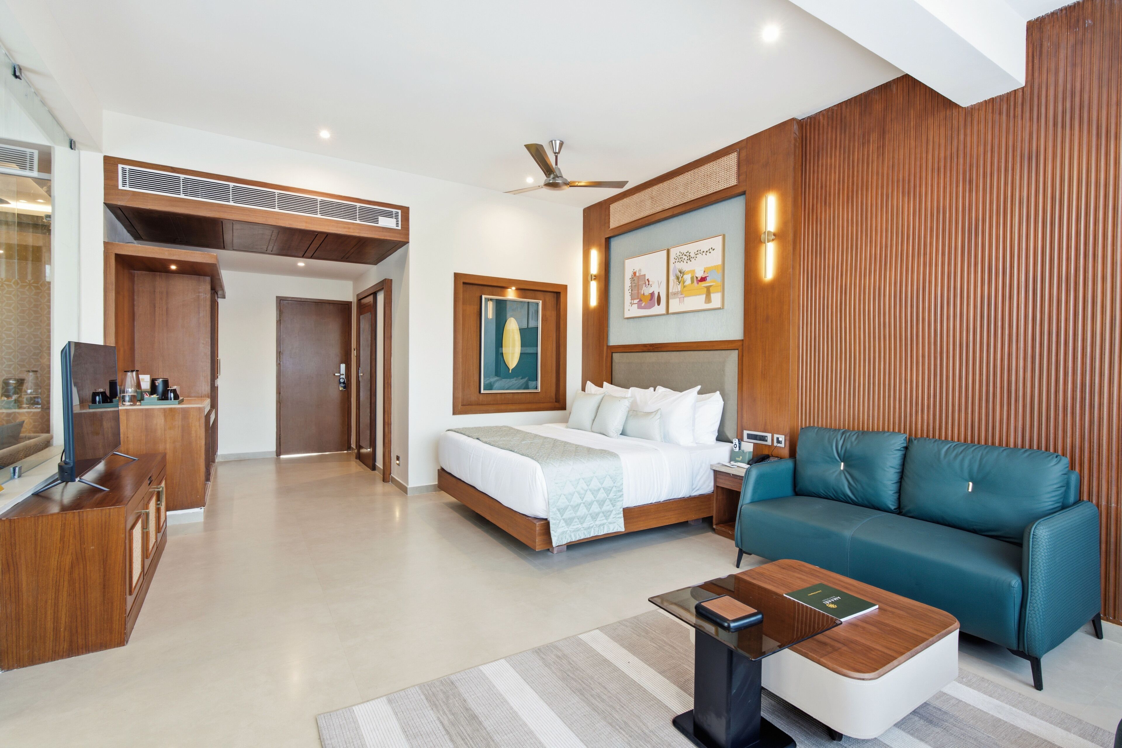 A modern hotel room with a bed, a sofa, a desk, and a ceiling fan.