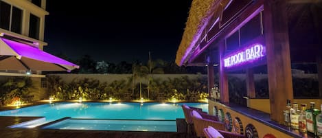 Eine Poolbar mit Neonreklame, einer Holzterrasse, Liegestühlen und einem Schwimmbecken.
