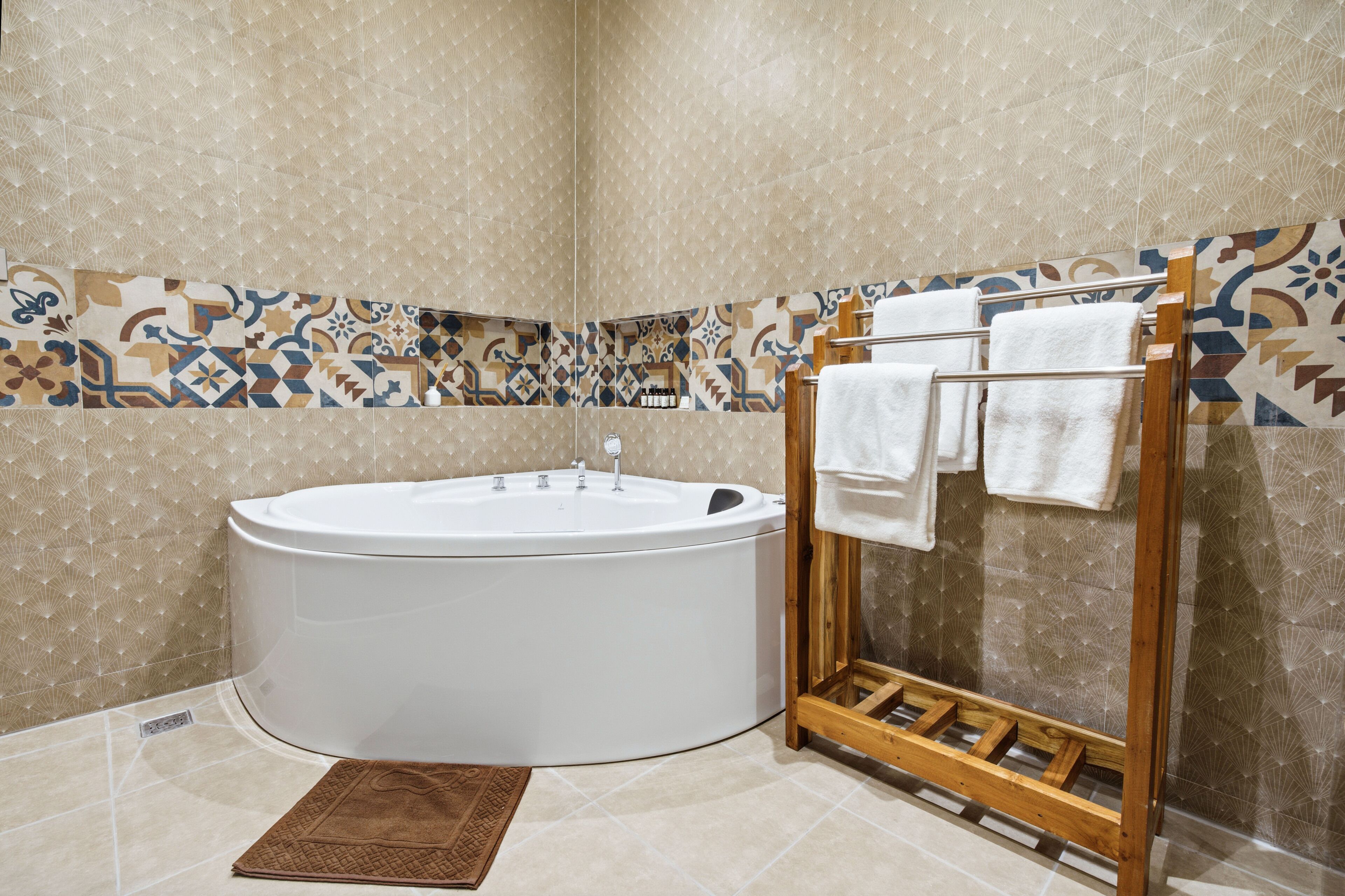 A bathroom with a freestanding bathtub, a wooden towel rack, and patterned wall tiles.