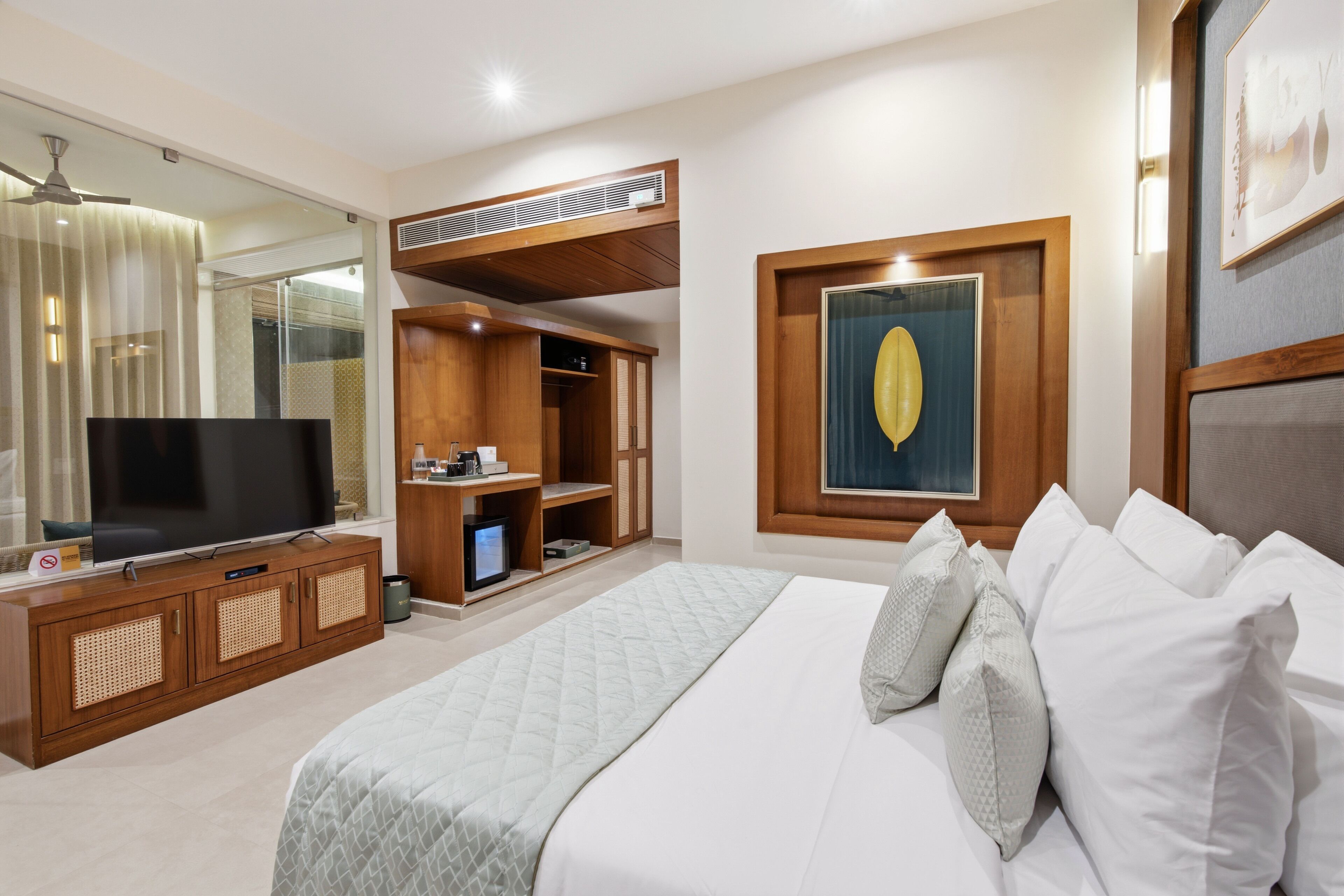 Habitación de hotel con cama, televisión, armario y un amplio ventanal.