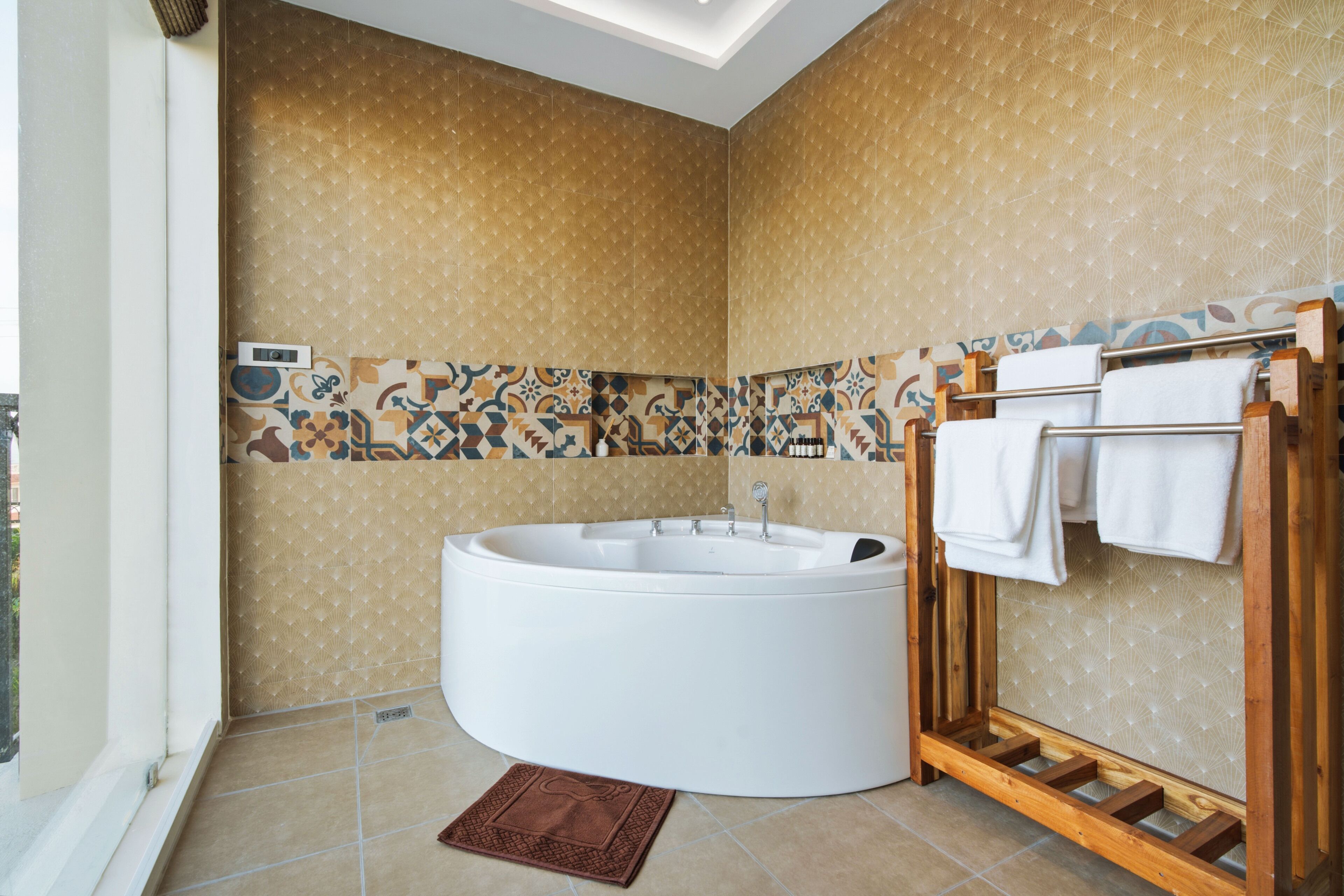 Une salle de bain avec une baignoire sur pieds, un porte-serviettes en bois, des carreaux à motifs et un tapis marron.