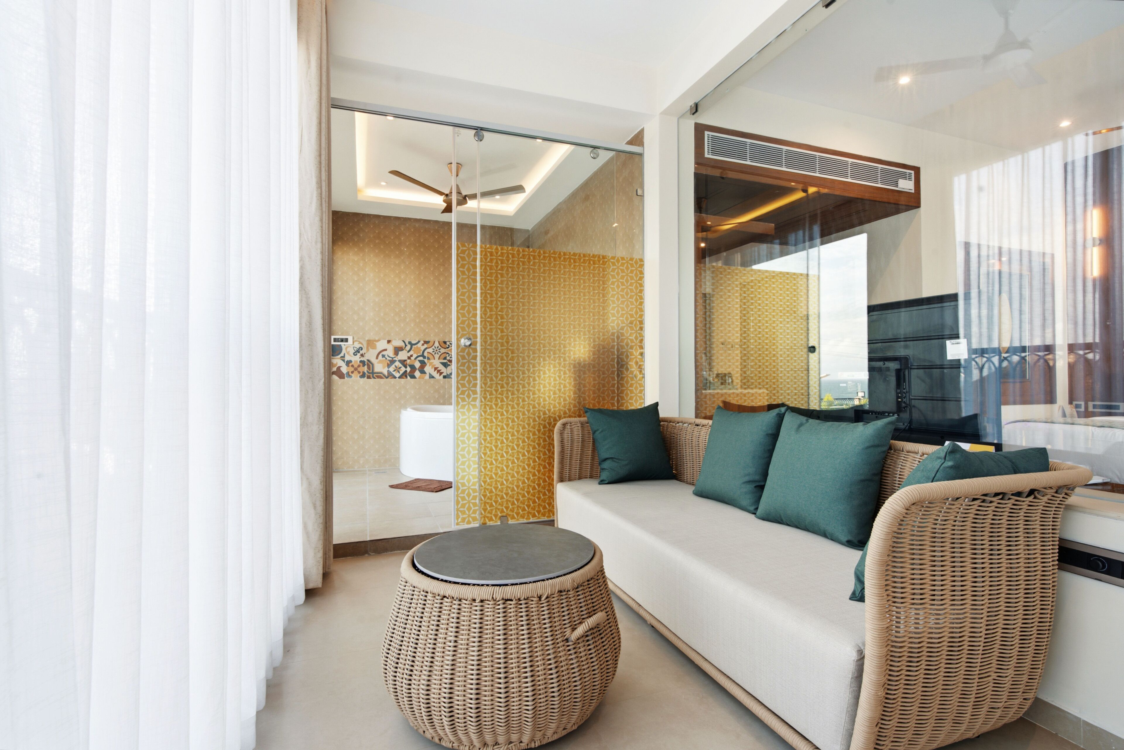Un espace de vie moderne comprenant un canapé, un pouf en osier et une cloison en verre.