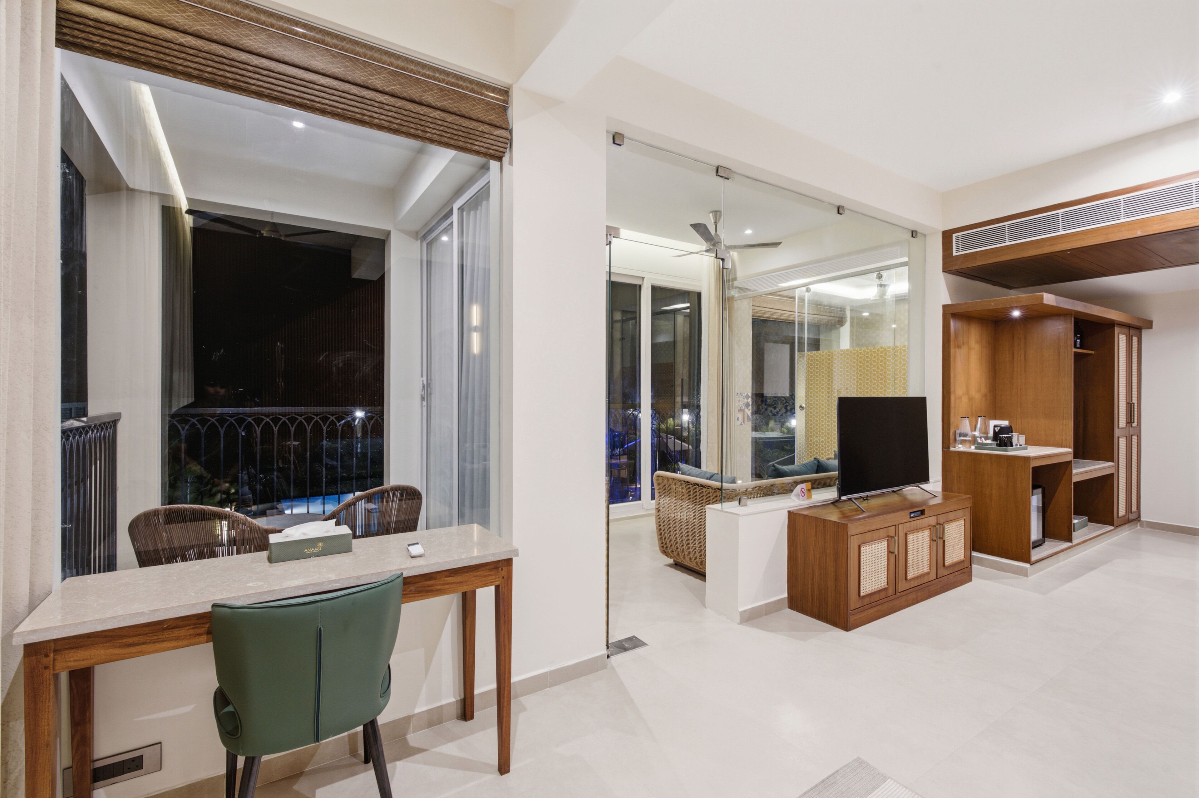 A modern living room with a dining area, a flat-screen TV, and a balcony with a view.
