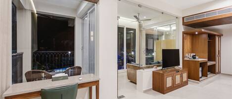 A modern living room with a dining area, a flat-screen TV, and a balcony with a view.