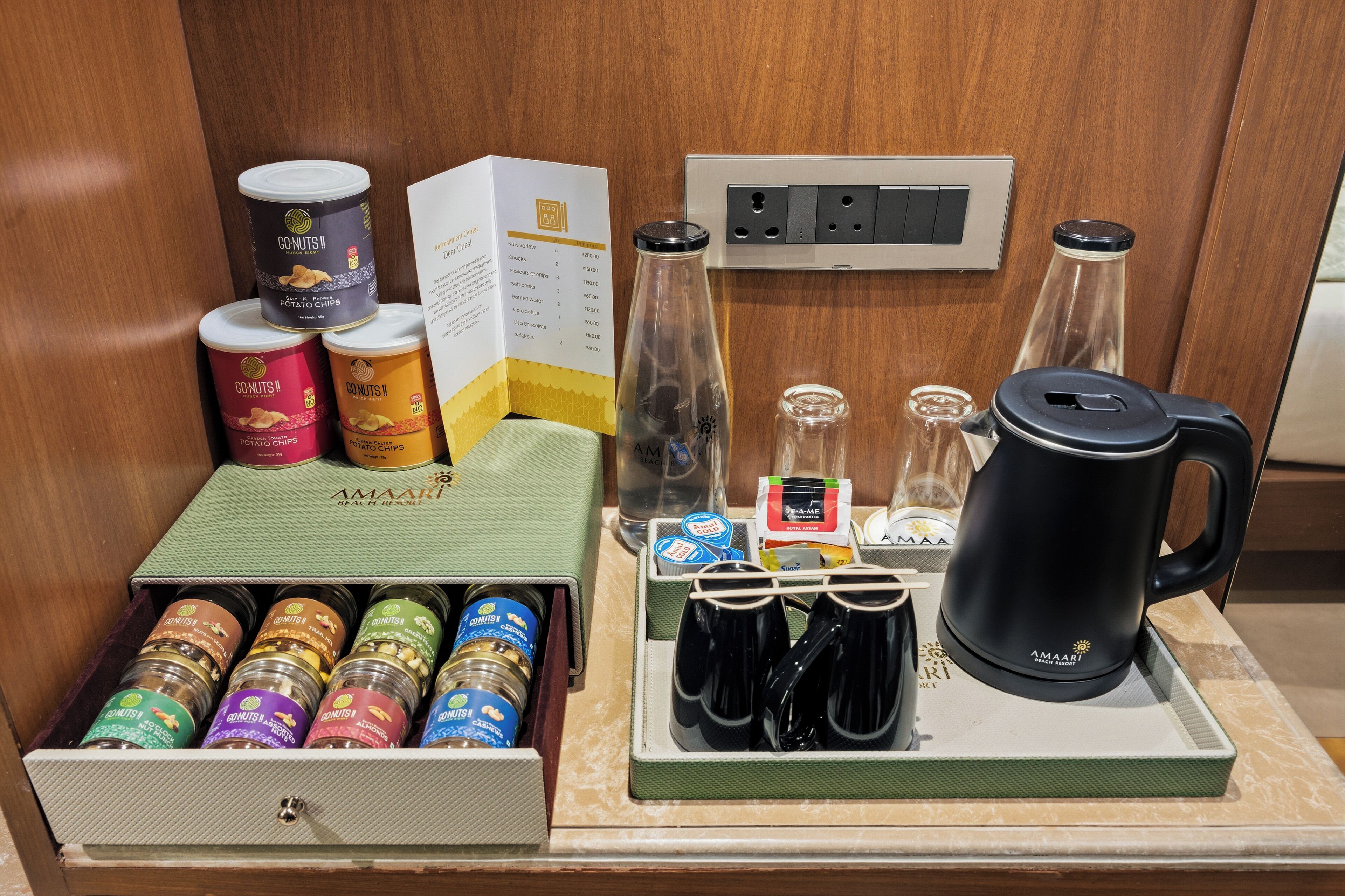 A minibar setup with various food items, a coffee maker, and a bottle of water.