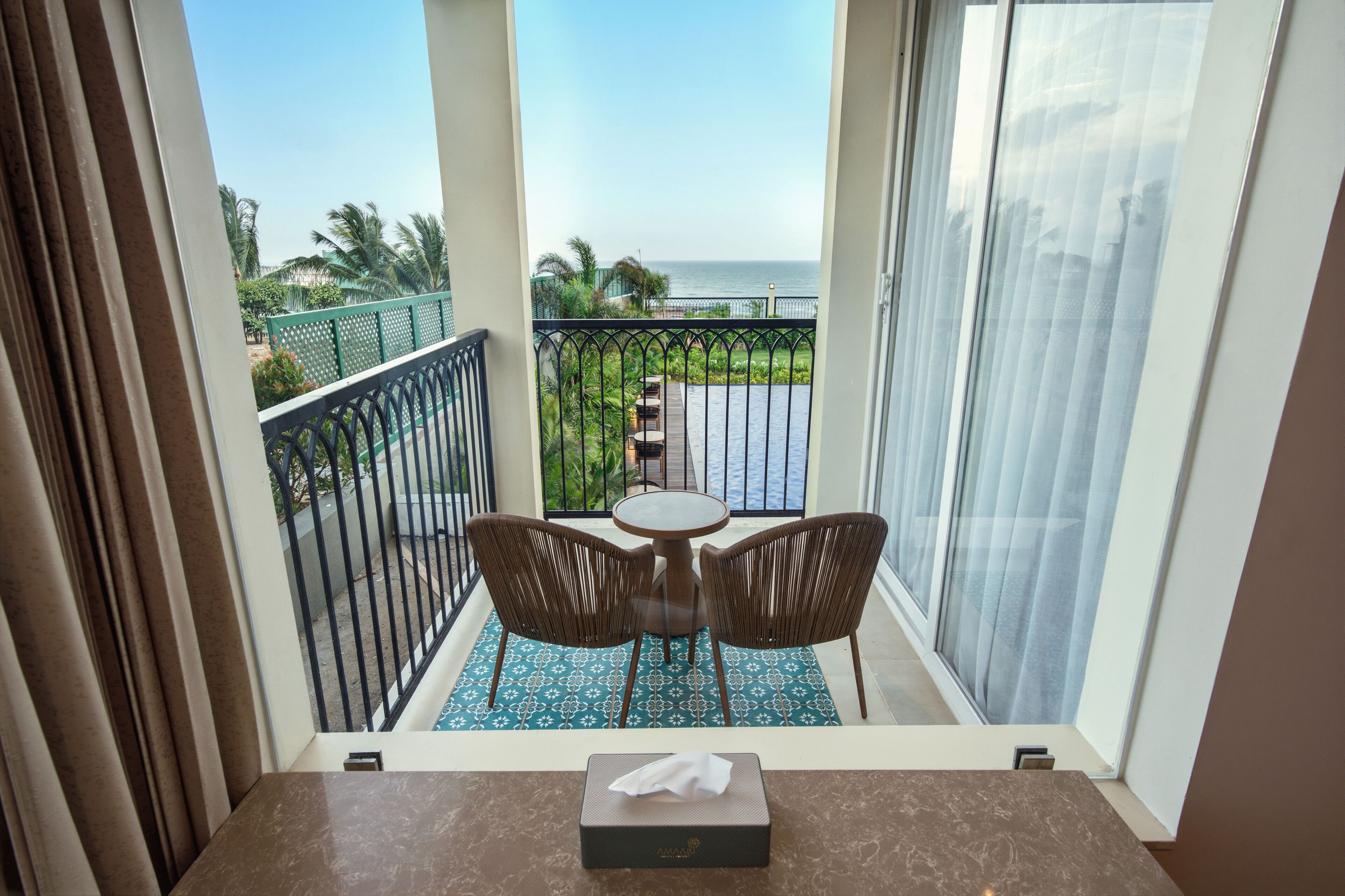 A balcony with a table and chairs, a view of the sea, and a tropical garden.