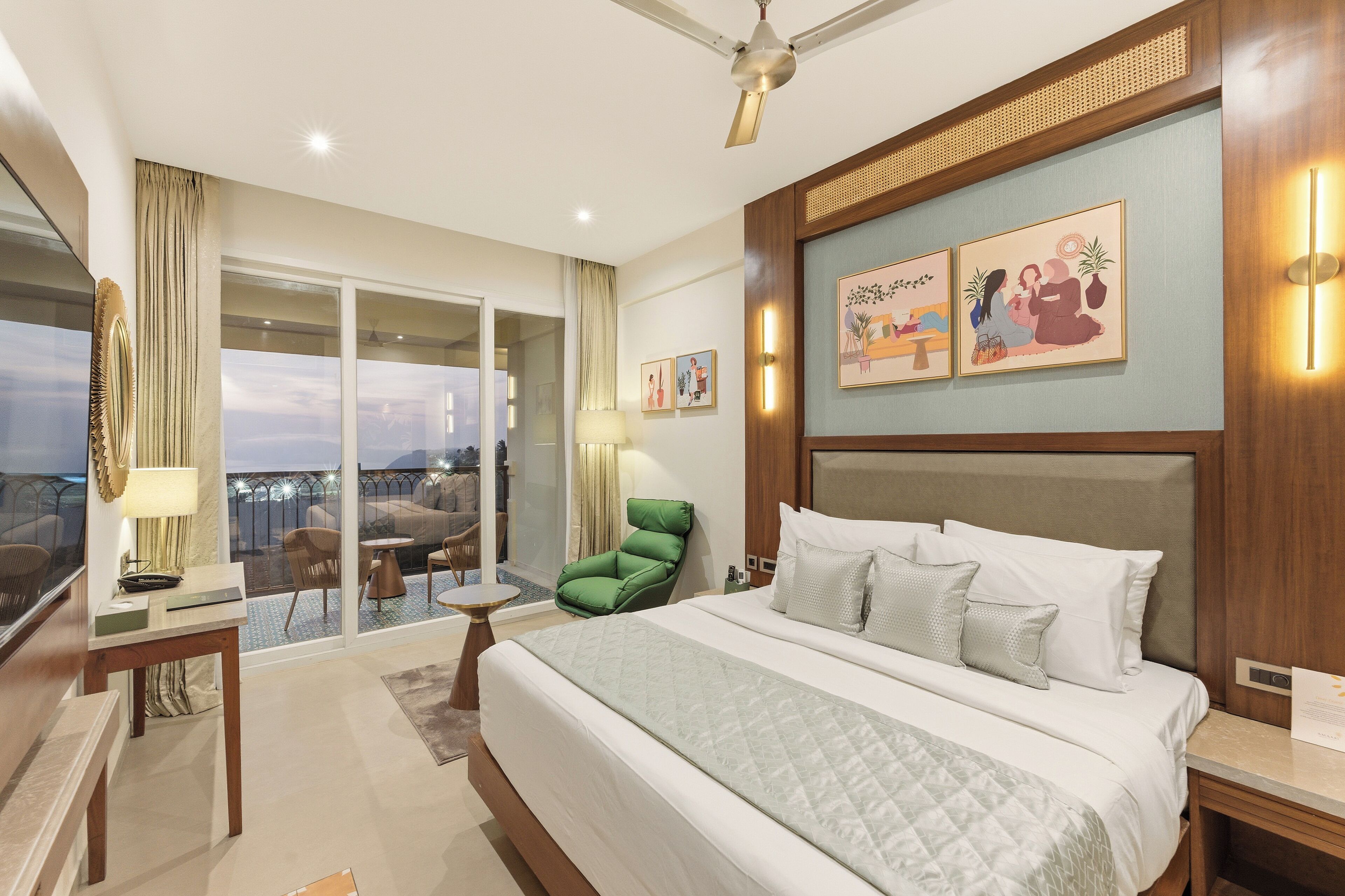 Une chambre d’hôtel avec un grand lit, un fauteuil vert, un balcon avec vue et des œuvres d’art accrochées aux murs.