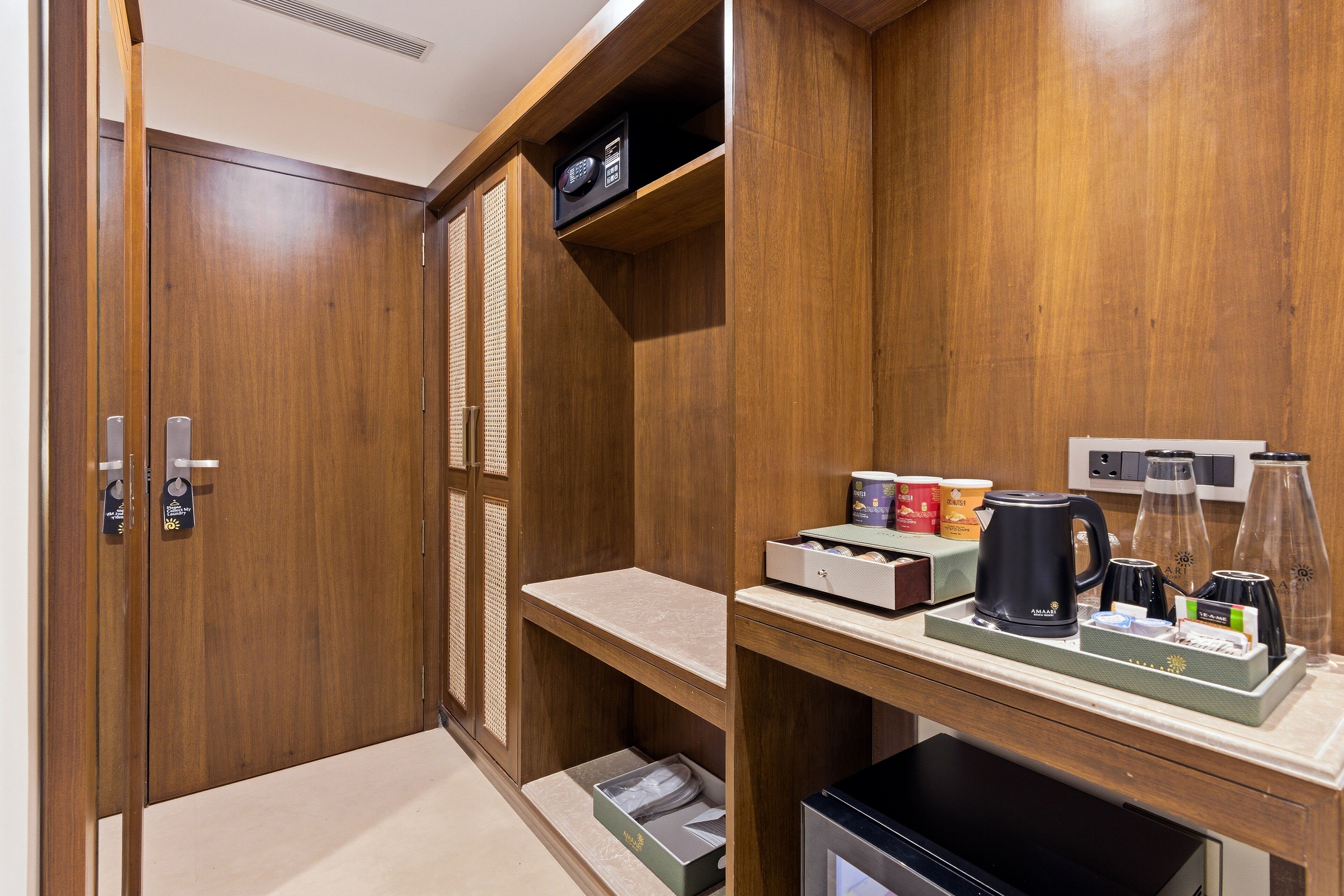 A wooden closet with a shelf containing a radio, a kettle, and a coffee maker.