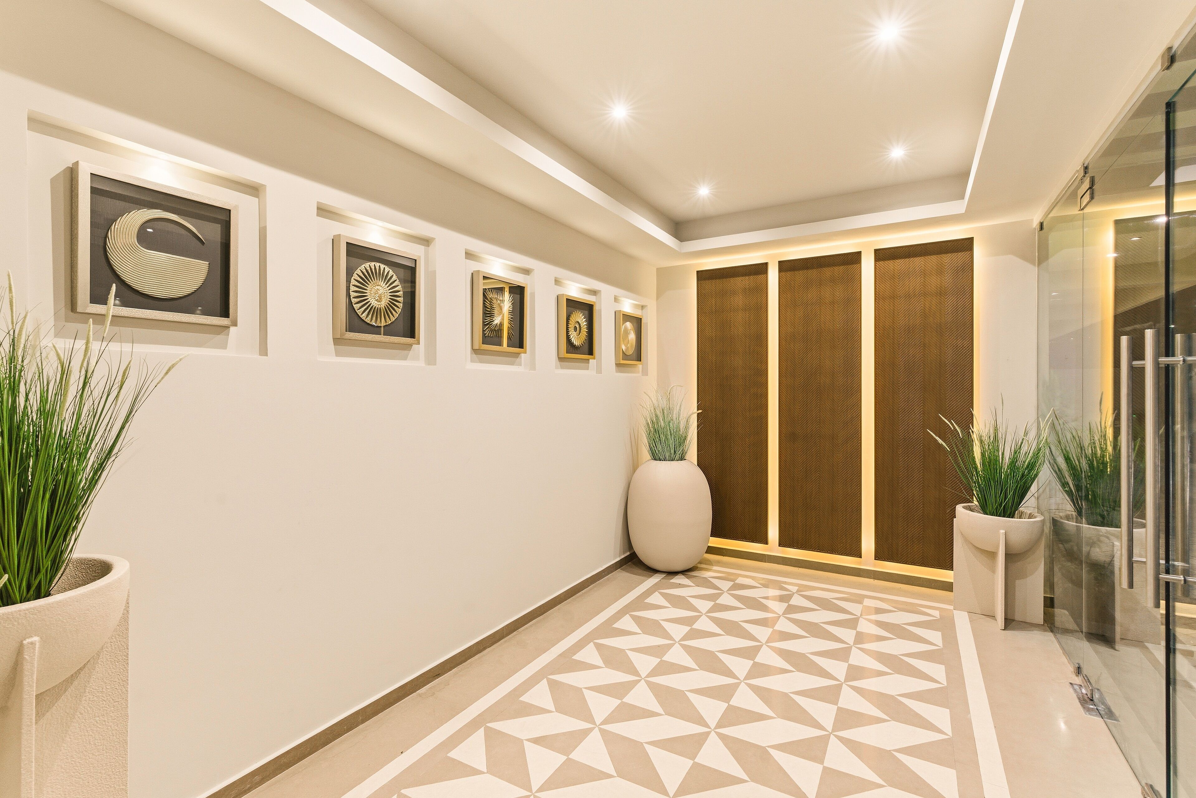 A modern hallway with geometric patterned flooring, wall-mounted art, and potted plants.