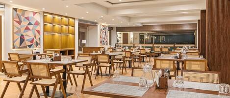 A spacious dining area with multiple tables and chairs, wooden paneling on the walls, and geometric artwork on the walls.