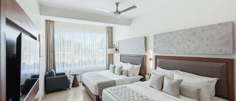 A hotel room with two beds, a TV, a ceiling fan, and a large window with curtains.