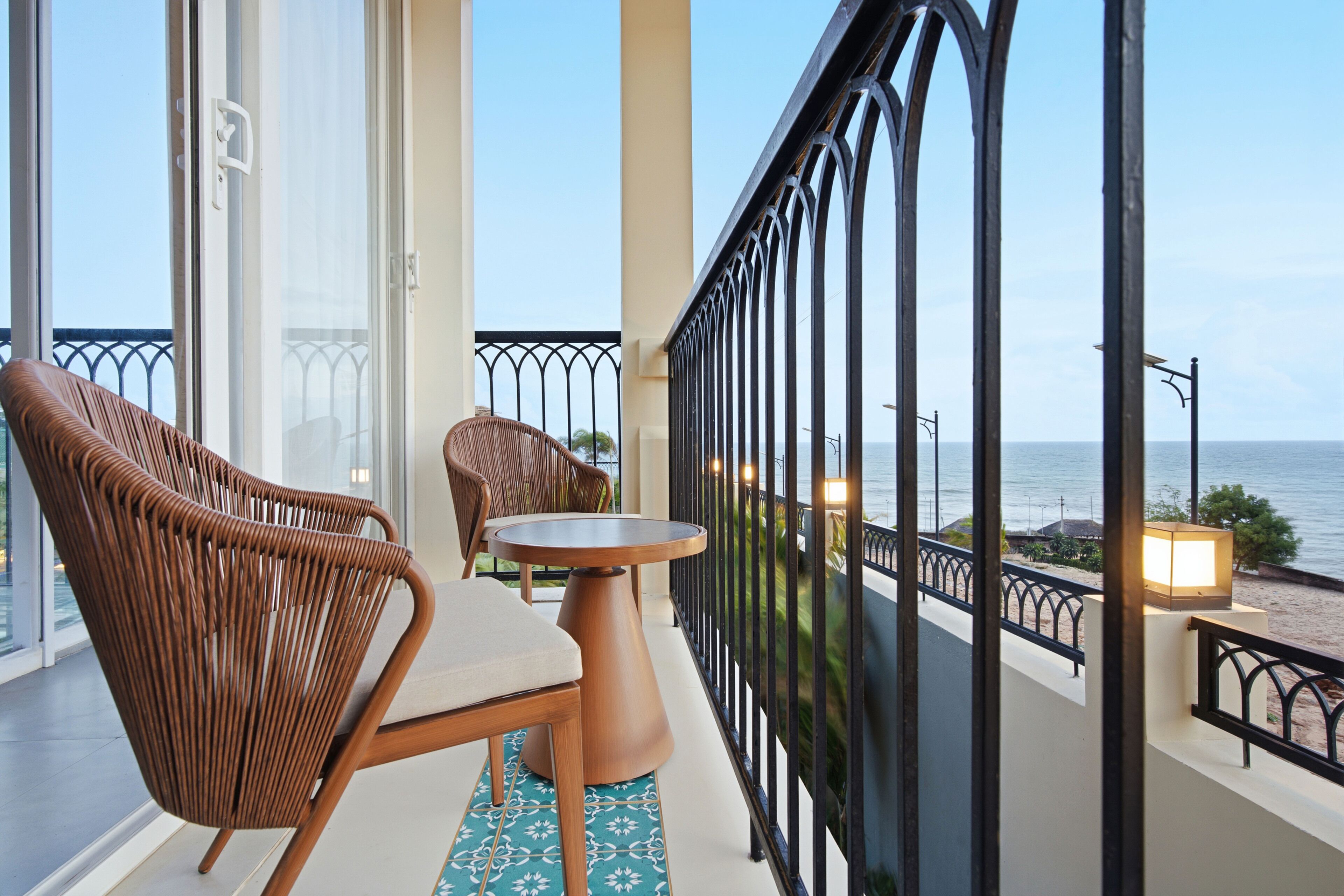 Un balcon avec des fauteuils en osier, une petite table ronde et une vue sur la mer.