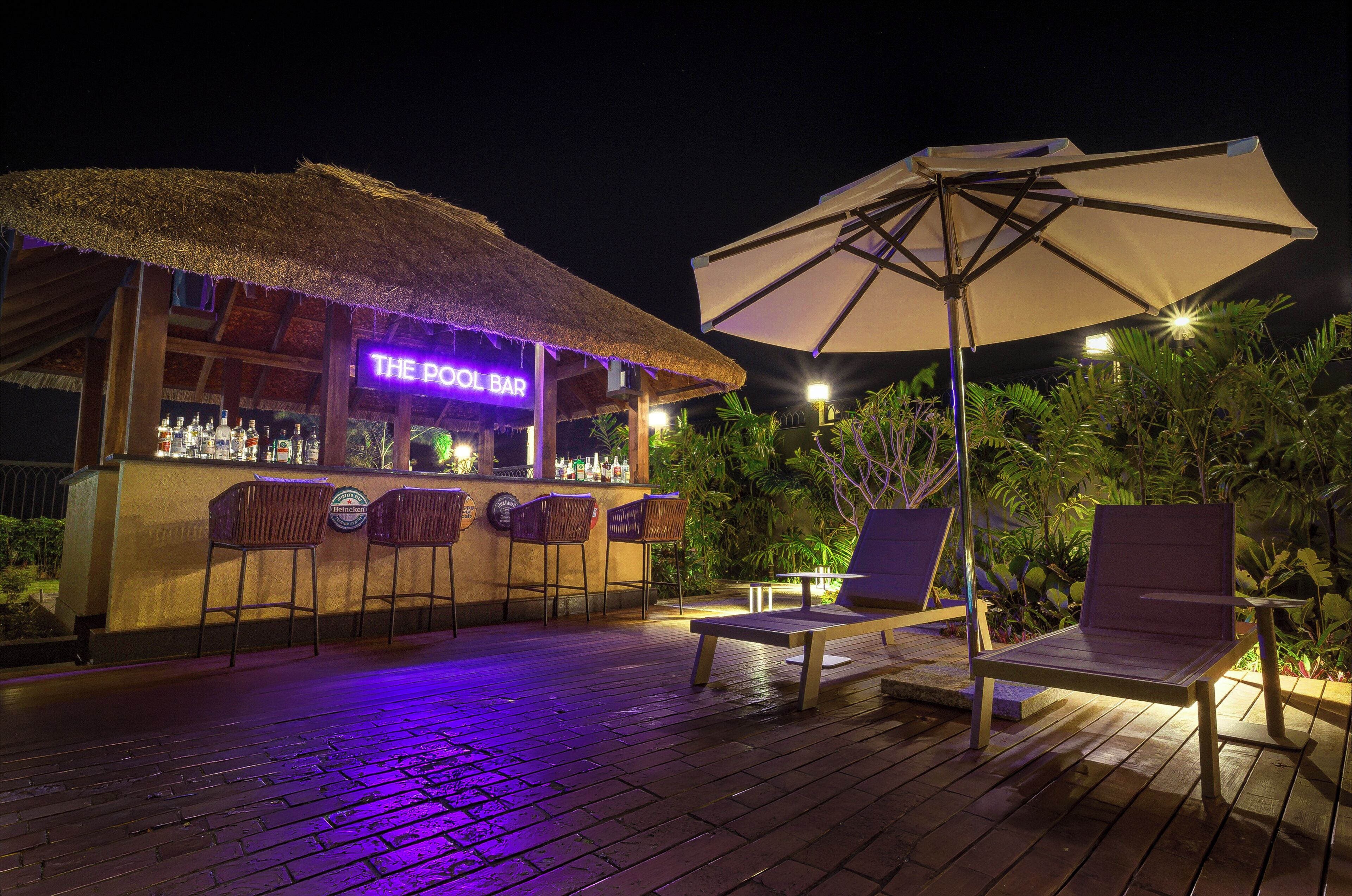 Zona de bar con un letrero de neón, asientos al aire libre y techo de paja.