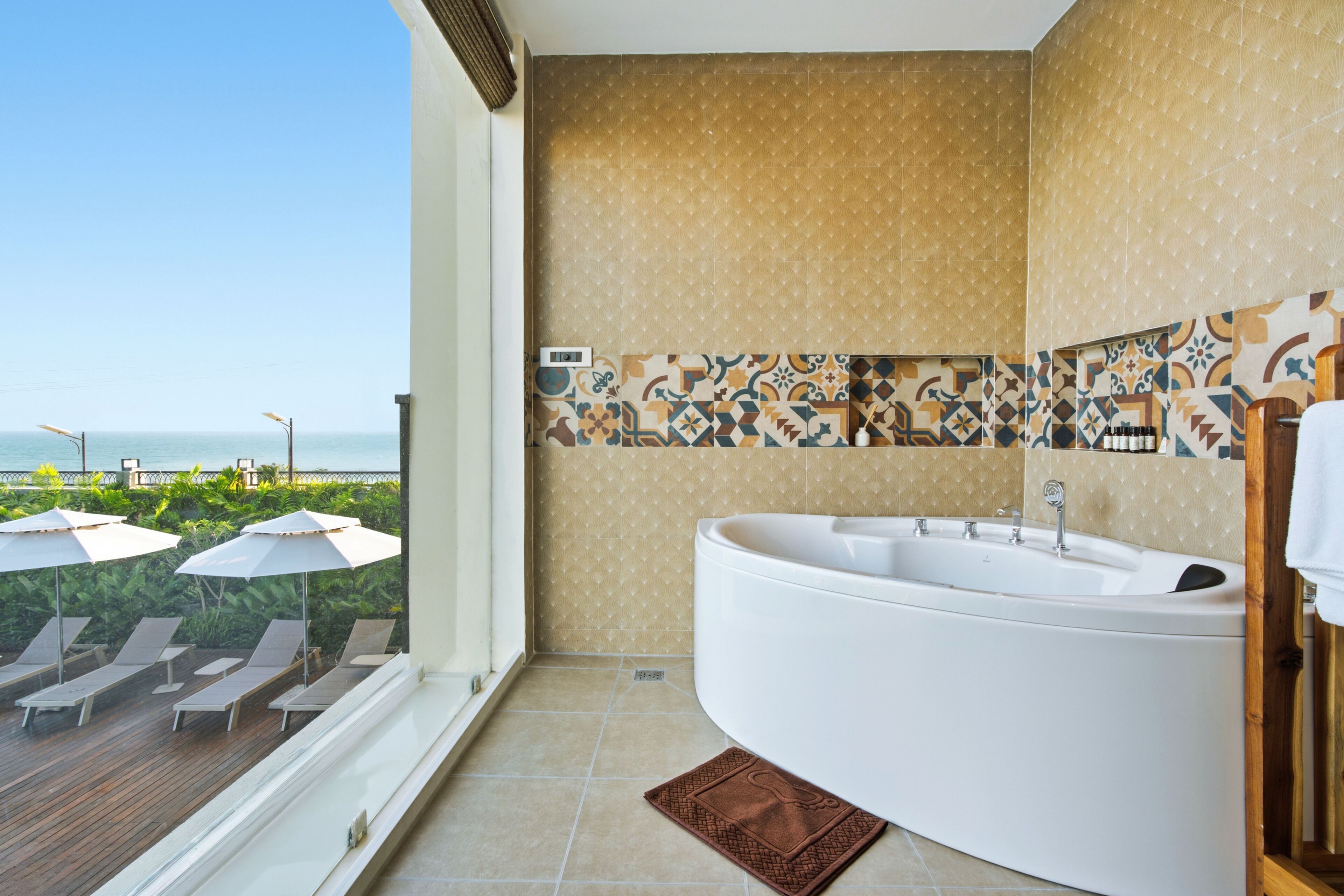 A bathroom with a large bathtub, a window with a view of the sea, and a tiled backsplash.