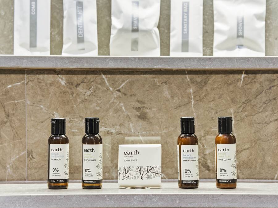 Fire flasker Earth produkter står på en hylde, herunder shampoo, brusegel, badesæbe og bodylotion, mod en marmorbaggrund.
