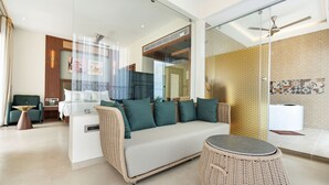 Moderni hotellihuone, jossa on sohva, pyöreä pöytä, tuoli, sänky ja lasiseinä.
