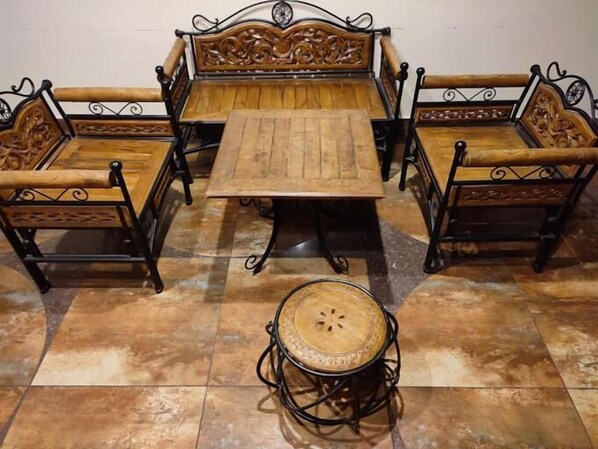 A wooden sofa set with intricate carvings, a matching wooden table, and a small round table with a woven top.