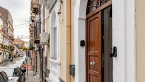 Una stretta via con auto parcheggiate e un edificio con una porta in legno e una finestra ad arco.