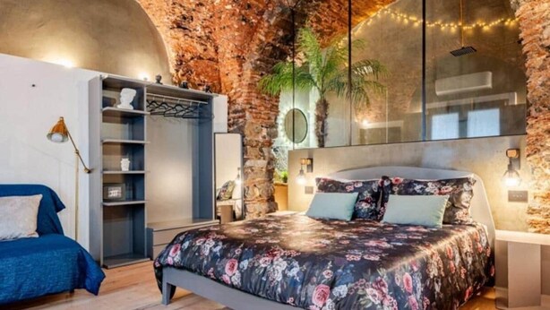 Una camera da letto con un letto, un armadio, uno specchio e una parete in pietra.