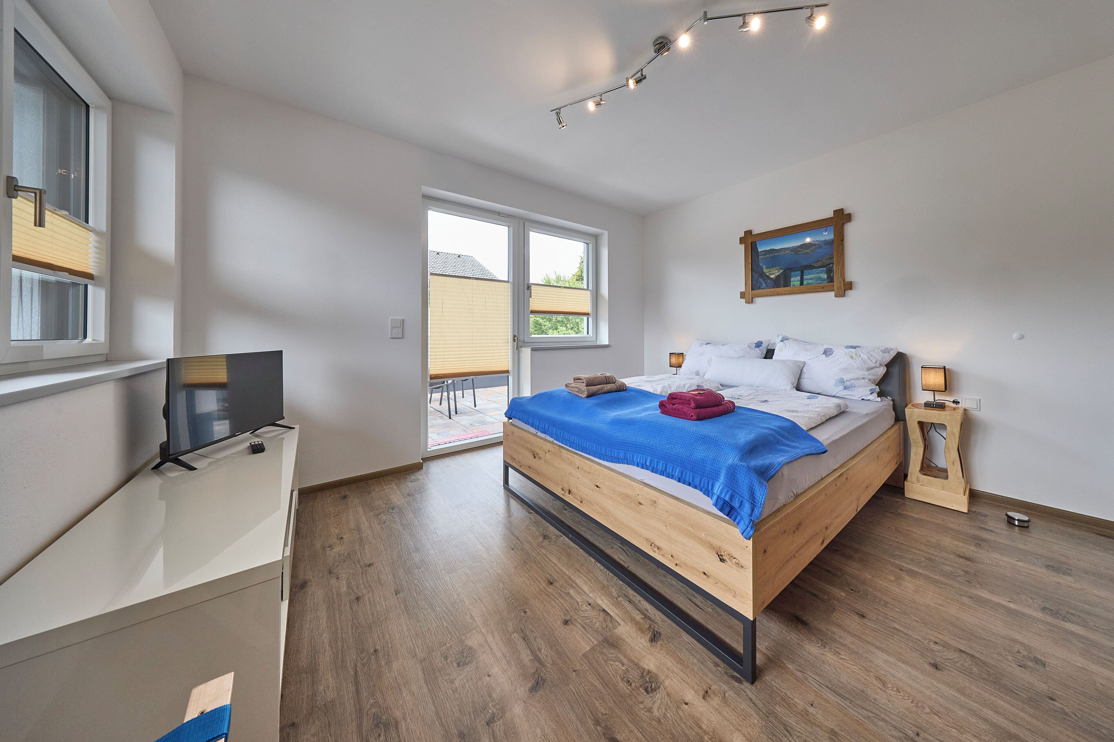 A bedroom with a bed, a TV, a window, and a painting on the wall.