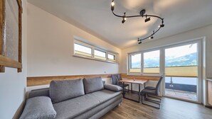 Una sala de estar moderna con sofá, mesa de comedor, sillas y ventanas amplias que ofrecen una vista.