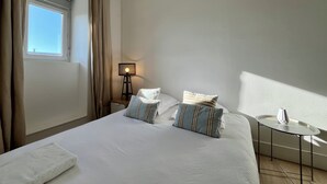 A bedroom with a bed, pillows, a bedside table, a lamp, and a window with curtains. - Chez MARIE - Central and Comfort (Valence)