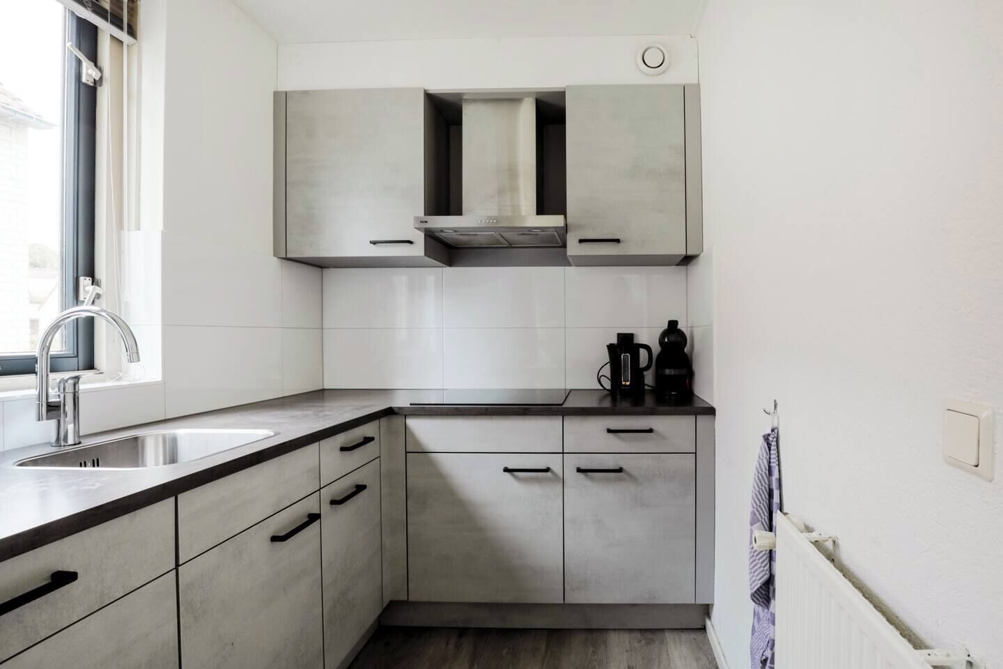 A modern kitchen with grey cabinets, a stainless steel sink, and a window providing natural light.