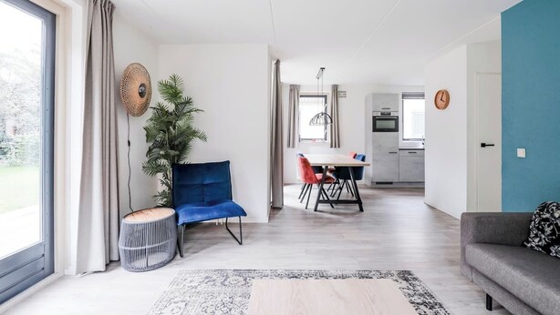 Un salon moderne avec un canapé bleu, un coin repas avec une table et des chaises, et une cuisine en arrière-plan.
