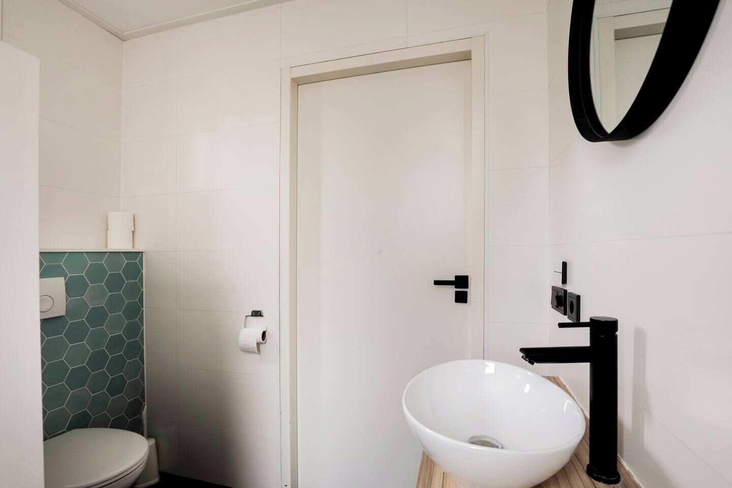 Ein Badezimmer mit Toilette, Waschbecken mit schwarzem Wasserhahn und einem Spiegel an der Wand.