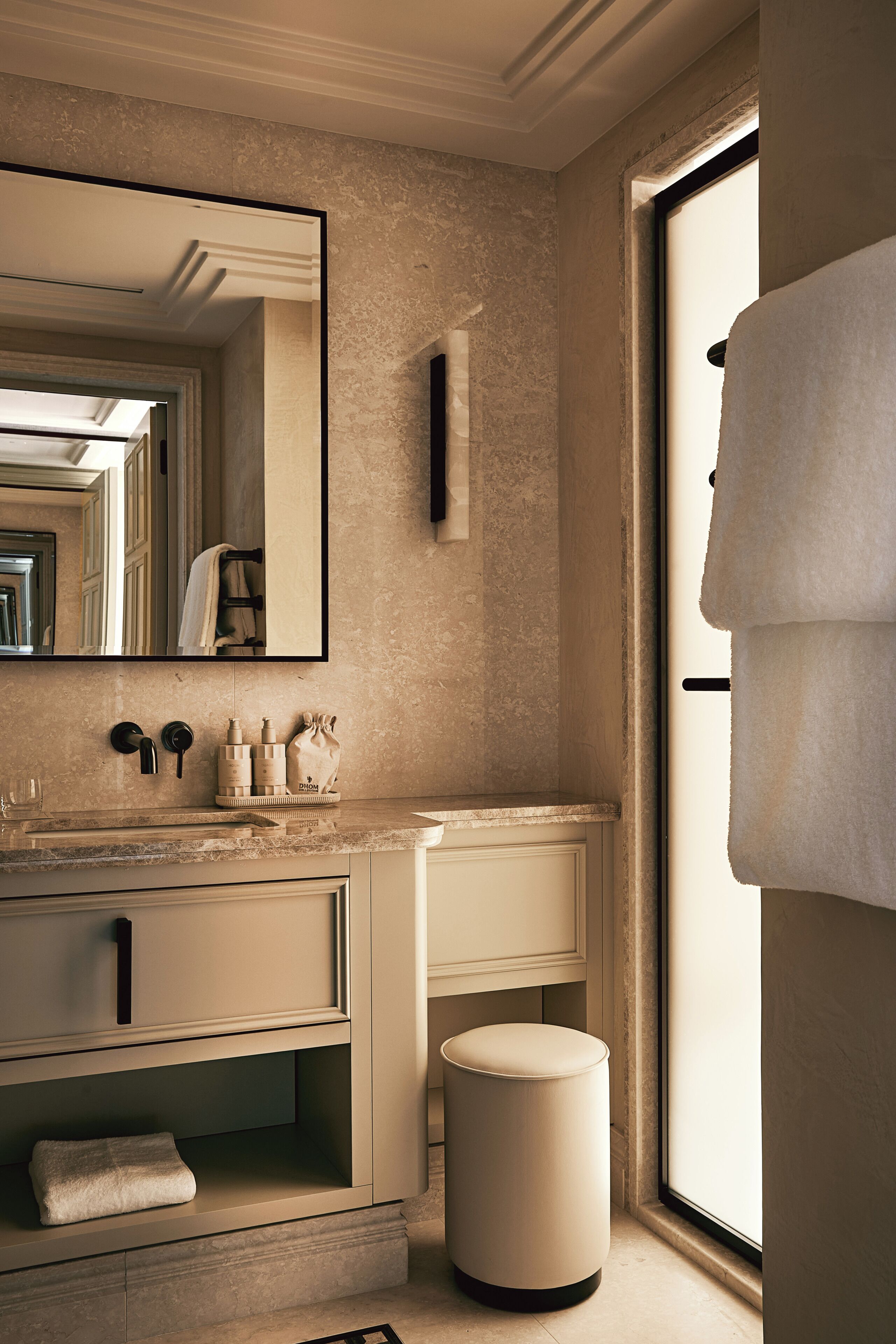 A bathroom with a large mirror, a sink with toiletries, a towel rack, and a window with a towel hanging.