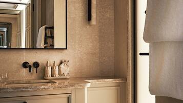 A bathroom with a large mirror, a sink with toiletries, a towel rack, and a window with a towel hanging.