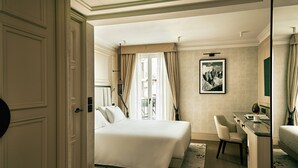 A hotel room with a large bed, a desk with a chair, a mirror, and a framed picture on the wall. - Grand Hotel Ampezzo (Cortina d'Ampezzo)