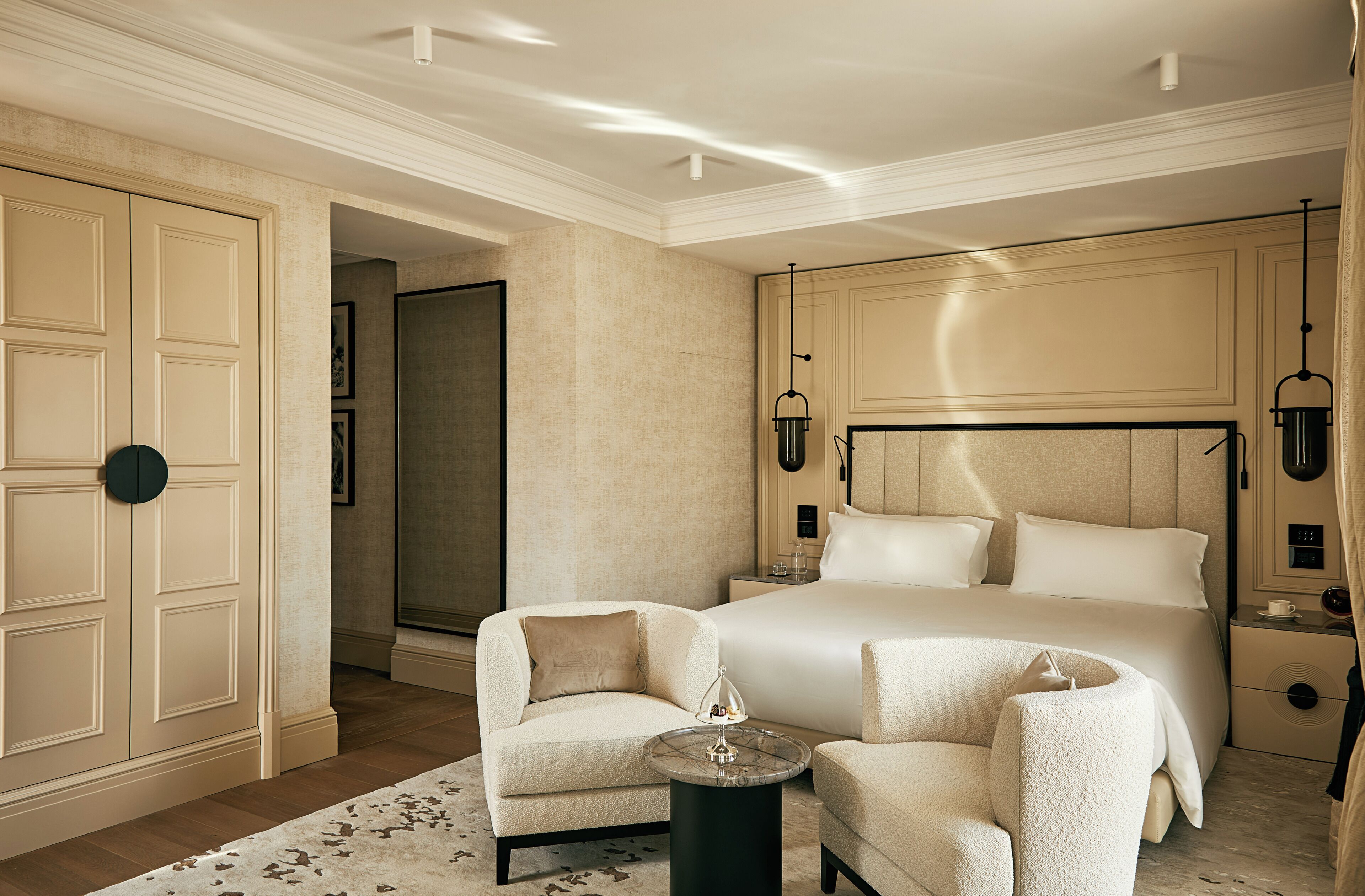 Una habitación de hotel con una cama grande, dos sillones, una mesita redonda y un minibar.