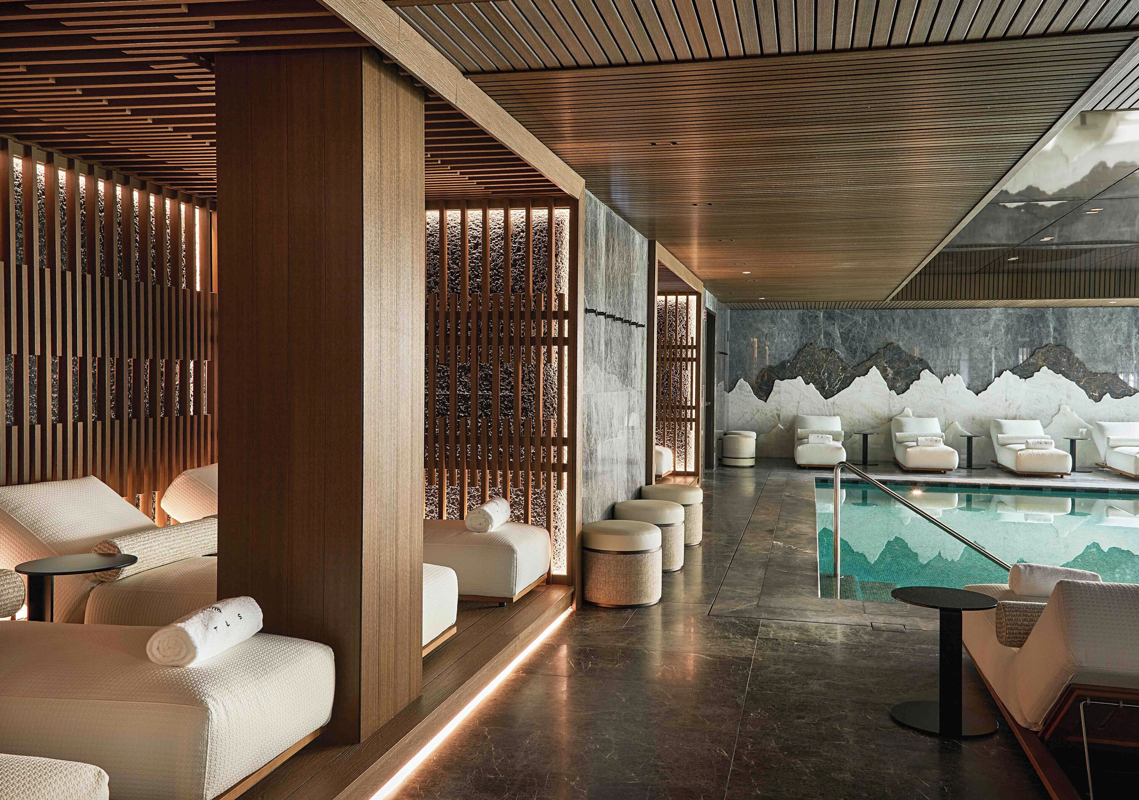 Un área de spa moderna con paneles de madera, una piscina con un mural de montañas y varias zonas de estar.
