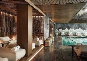 Un área de spa moderna con paneles de madera, una piscina con un mural de montañas y varias zonas de estar.