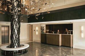 A reception area with a modern design, featuring a reception desk, a large decorative tree, and a marble floor. - Grand Hotel Ampezzo (Cortina d'Ampezzo)