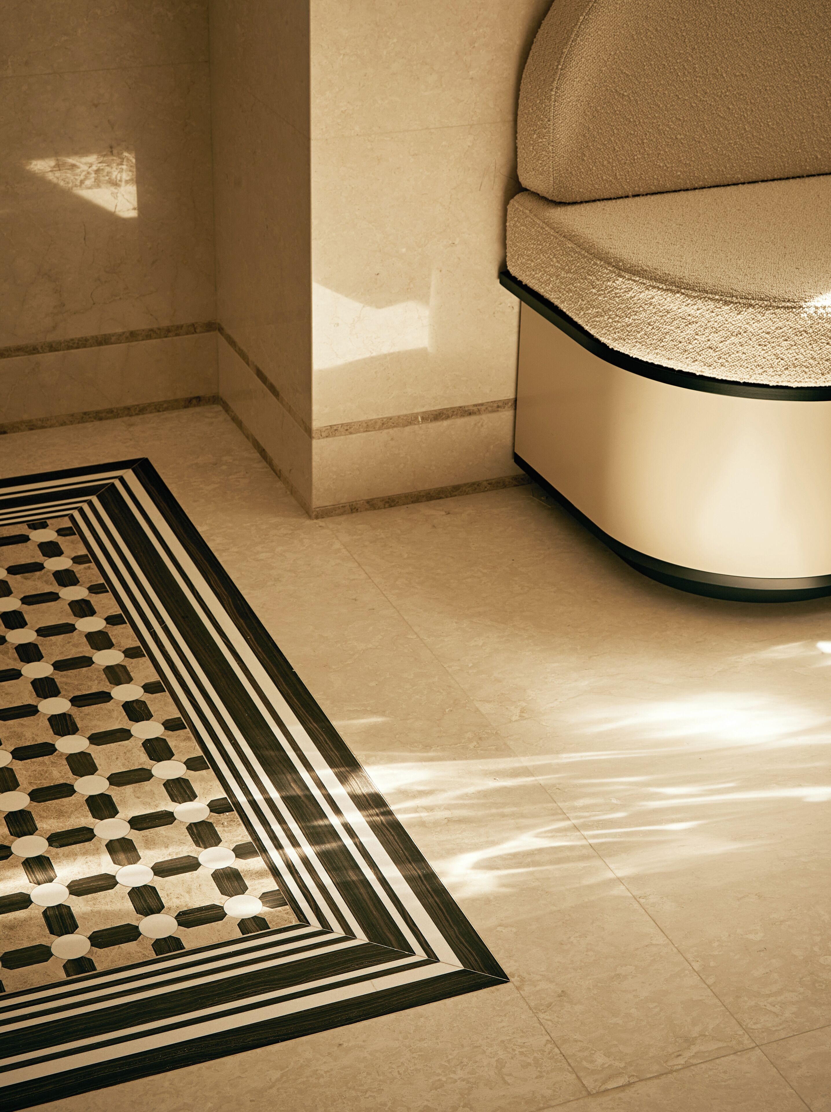 Un tapis à motifs posé sur un sol carrelé, un mur avec un revêtement texturé et un banc incurvé doté d’un siège rembourré.