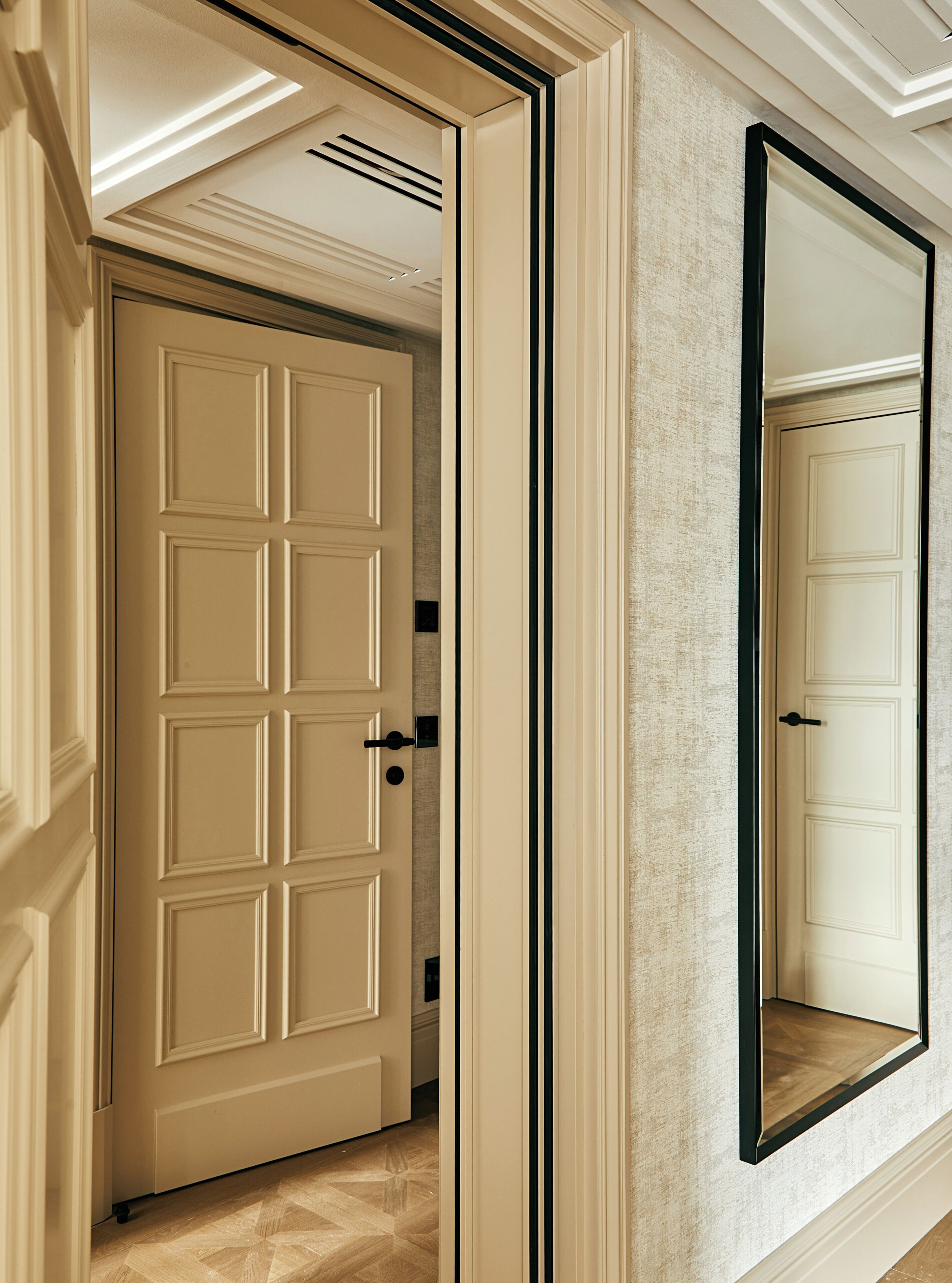 Un corridoio con una porta color crema, uno specchio con cornice nera e un muro dalla superficie strutturata.
