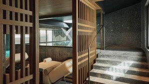 A modern interior with a wooden partition, a bed with a rolled-up towel, and a staircase leading to a dark wall. - Grand Hotel Ampezzo (Cortina d'Ampezzo)