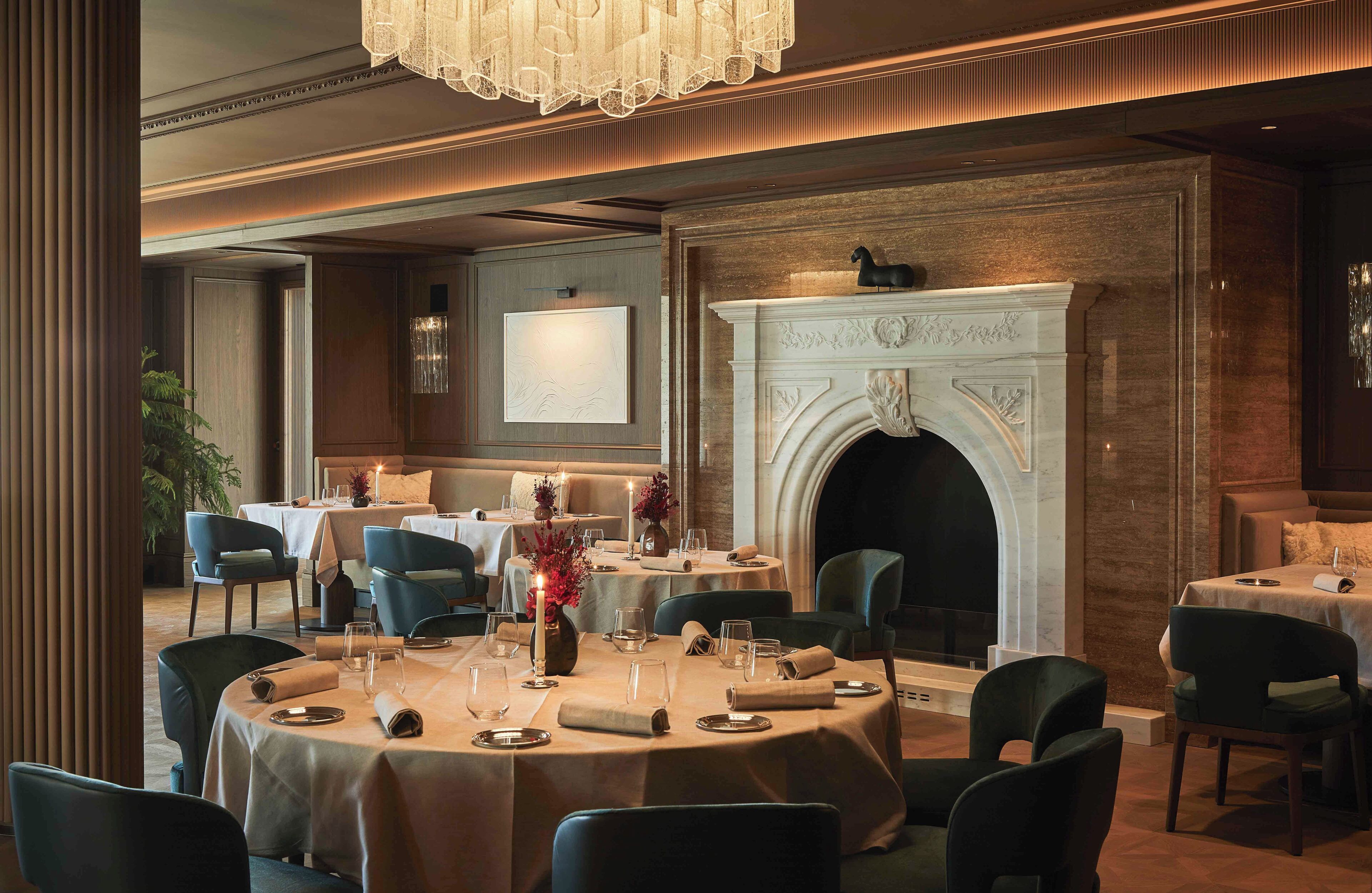 Un ristorante con tavoli rotondi, sedie, un camino e un lampadario.