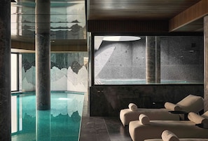 Ein Wellnessbereich mit Pool, Sitzgelegenheiten und einem großen Fenster zur strukturierten Wand.