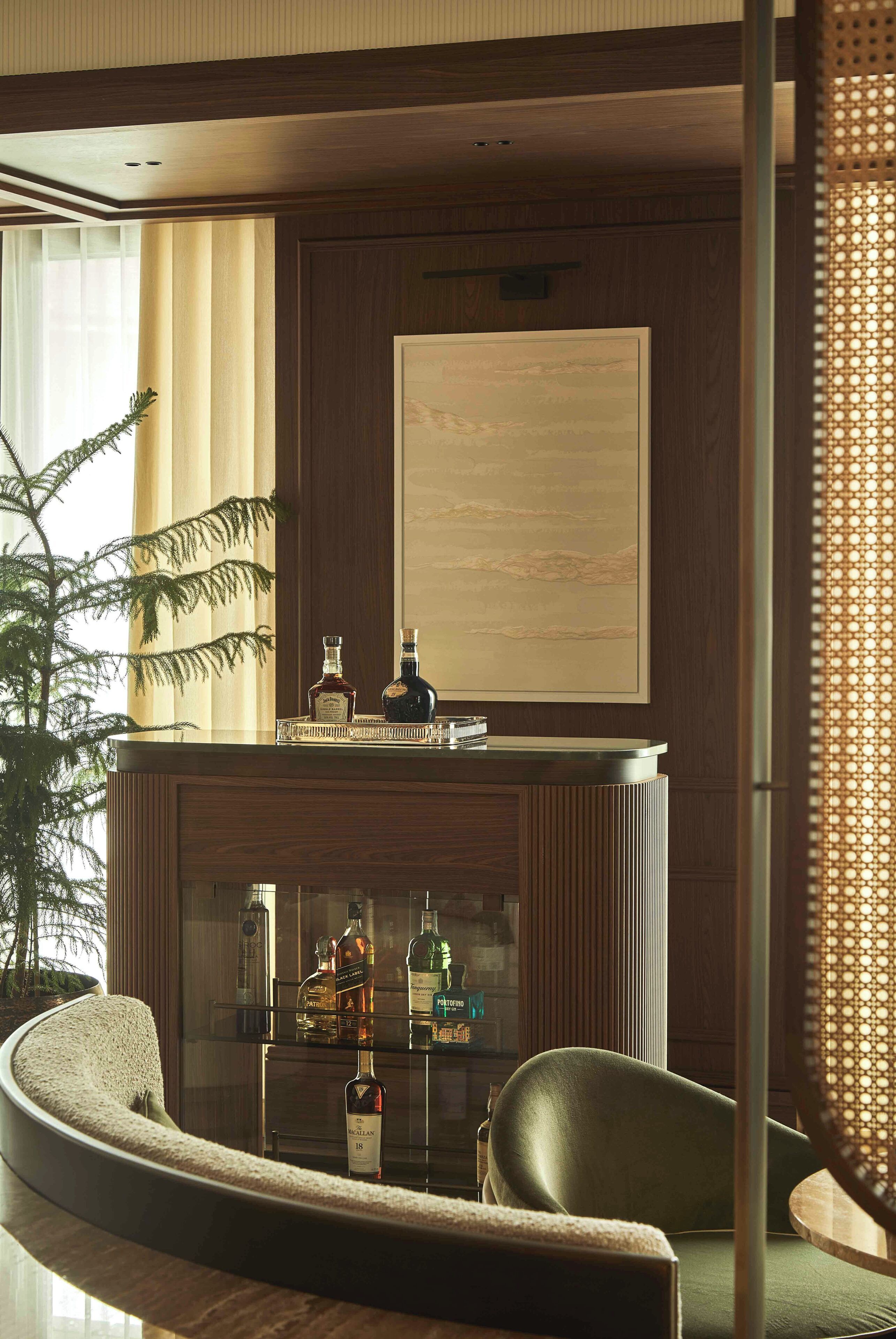 Un intérieur moderne avec un canapé aux lignes courbes, un mur recouvert de panneaux en bois et une vitrine en verre contenant diverses bouteilles.
